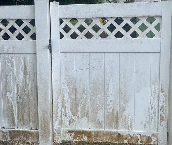 The same vinyl fence before, heavily streaked with brown and grey staining.